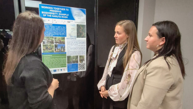 Trīs cilvēki apspriežas pie stenda referāta