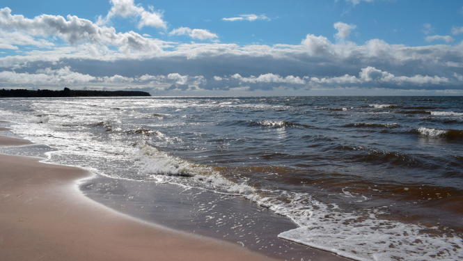 Jūras piekraste saulainā dienā ar mākoņainām debesīm
