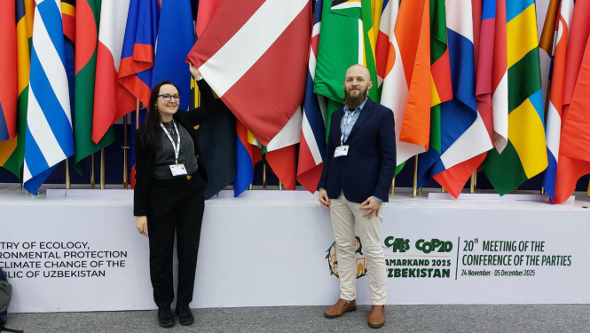 Sieviete un vīrietis pozē, fotografējoties uz daudzu valstu karogu fona.