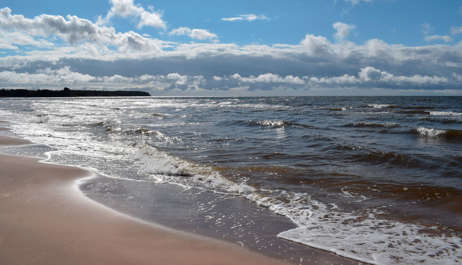 Jūras piekraste saulainā dienā ar mākoņainām debesīm