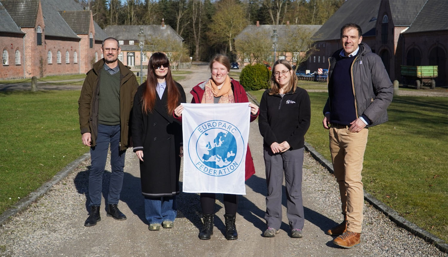 5 smaidoši cilvēki tur karogu ar EUROPARC logo